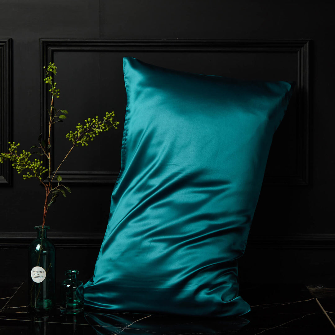 Teal silk pillowcase displayed upright against a dark background