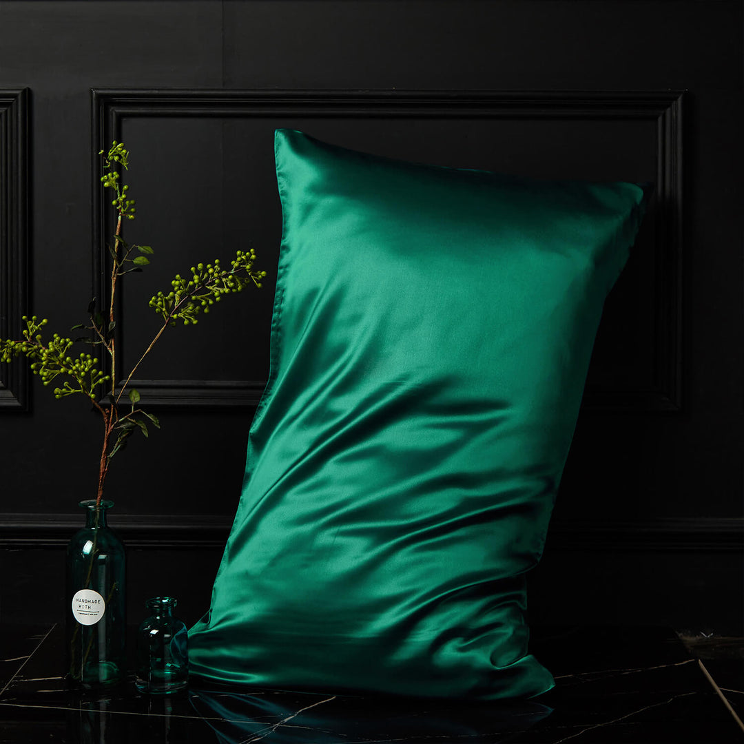Emerald green silk pillowcase displayed upright against a dark background